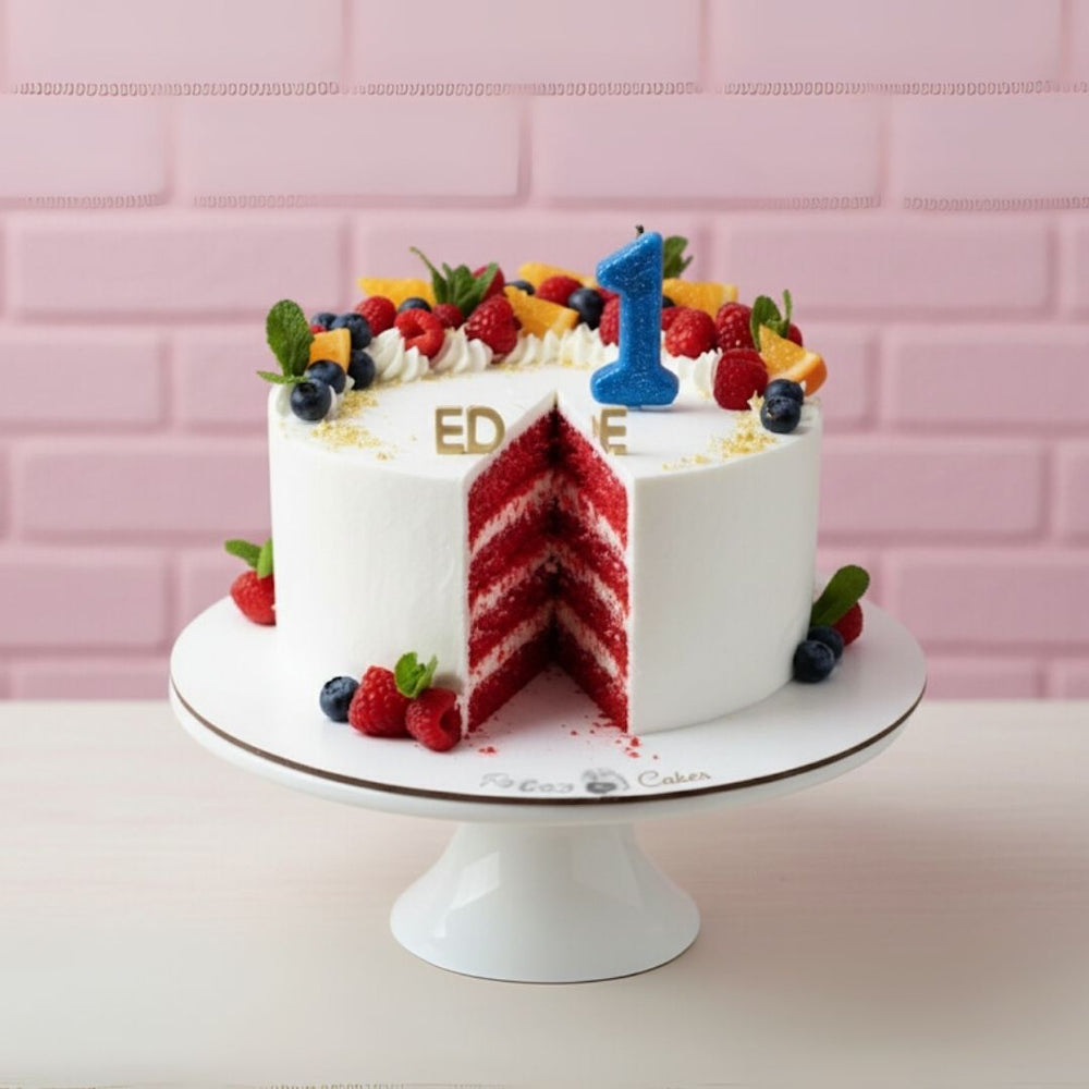 Red velvet cake with white frosting, berries, and a blue number '1' on a pink tiled background.