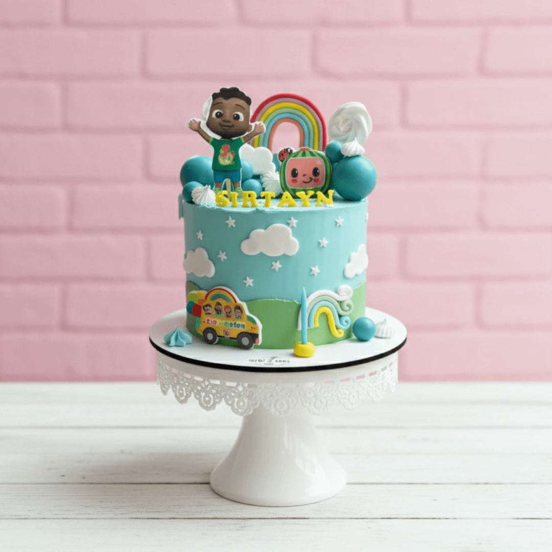 Cocomelon theme Colorful birthday cake with cartoon characters on a white stand against a pink brick wall.