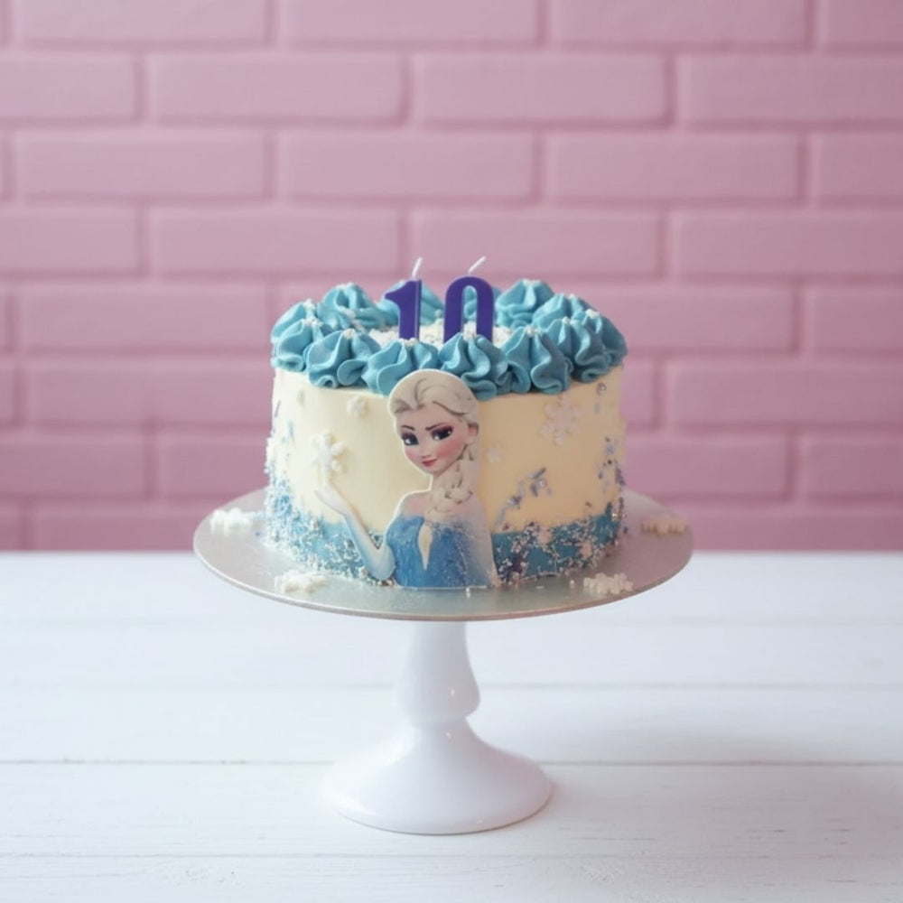 Elsa theme Birthday cake with blue frosting, a character, and number 10 candle on a pink brick wall background.