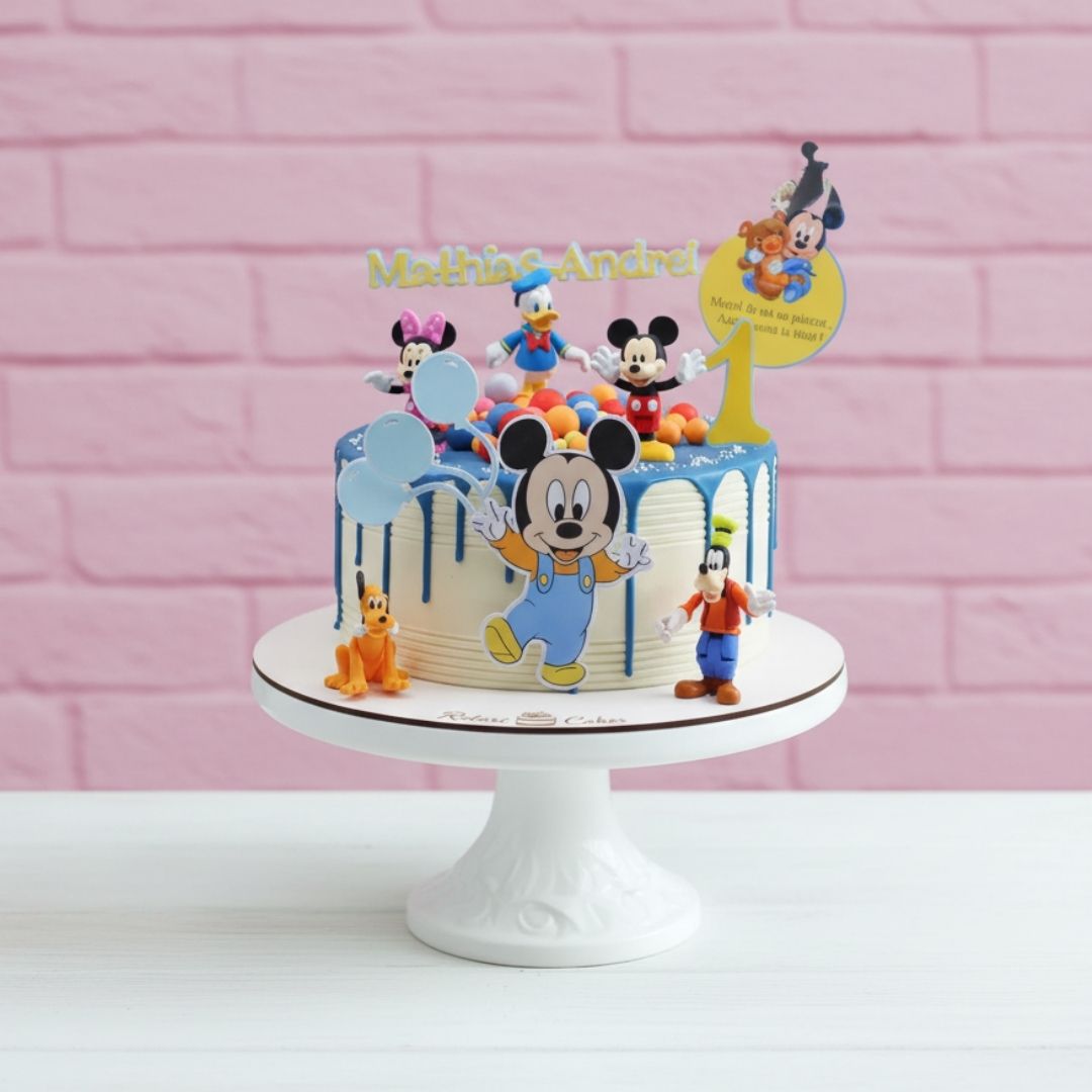 Mickey mouse theme Birthday cake with Mickey Mouse and friends on a white stand against a pink brick wall.