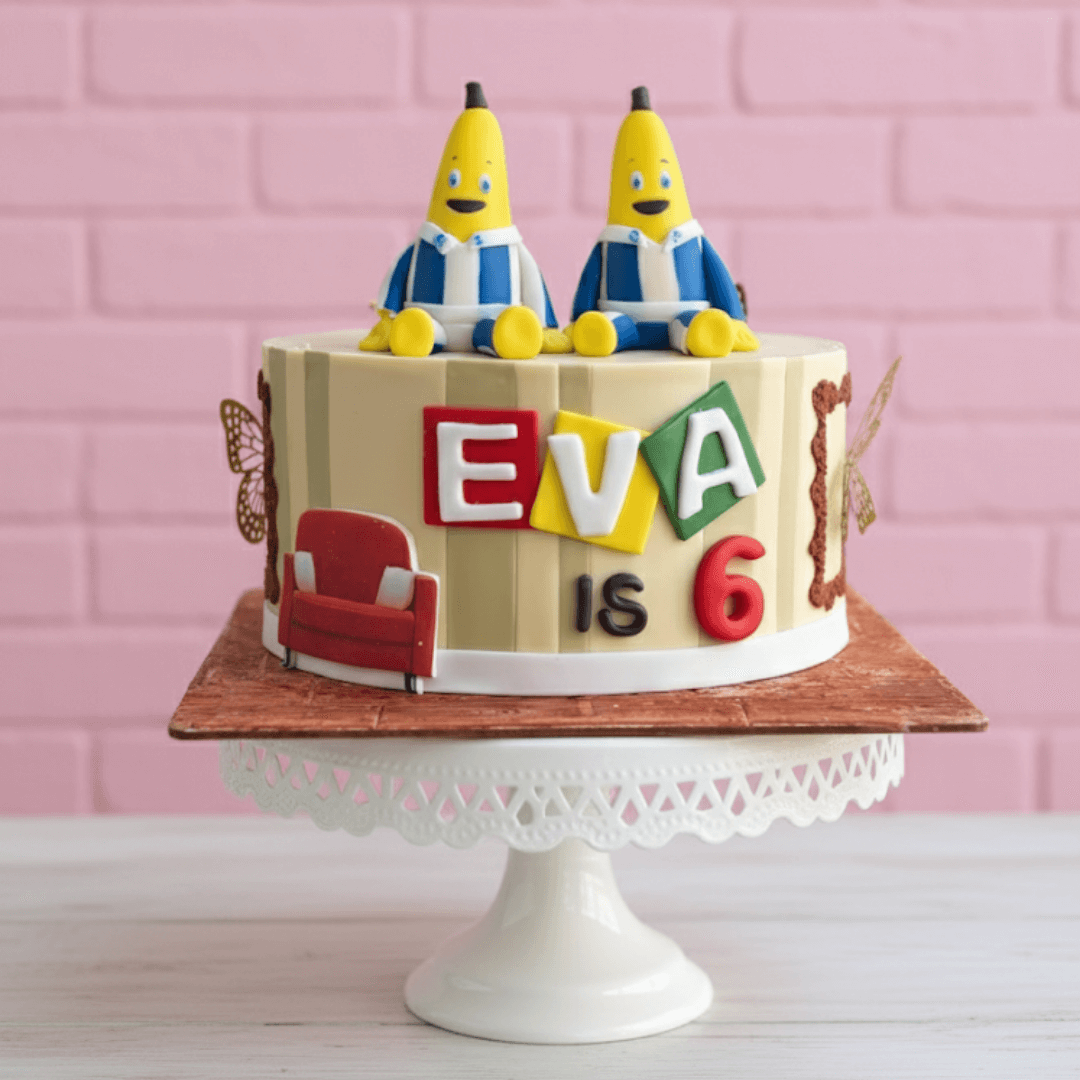 Birthday cake with bananas in pyjamas theme cartoon characters and 'EVA is 6' text on a pink brick wall background