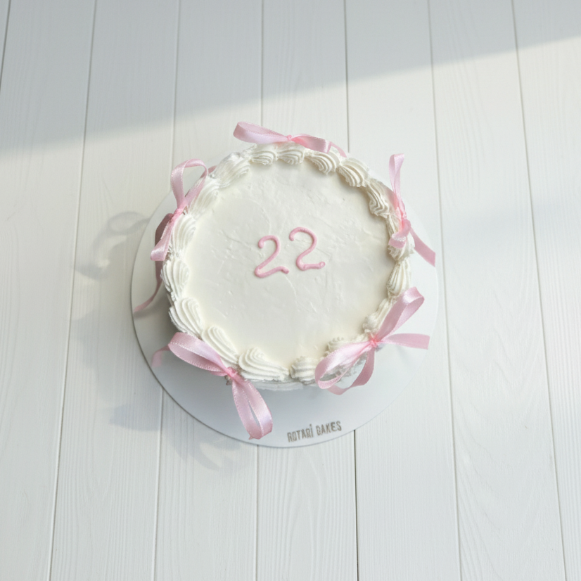 Small round cake with pink ribbons and number 22 on a white wooden surface