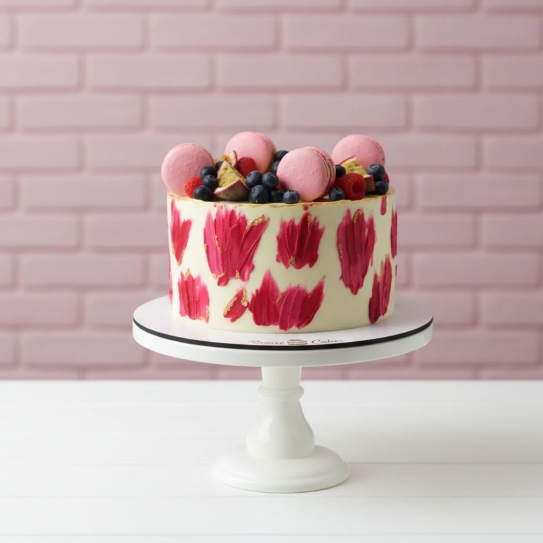 Cake with pink floral design on a white stand against a pink brick wall.