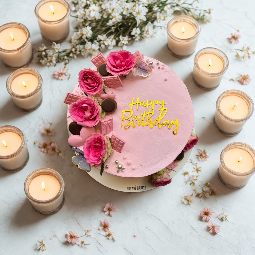 Pink birthday cake with flowers and candles on a light surface