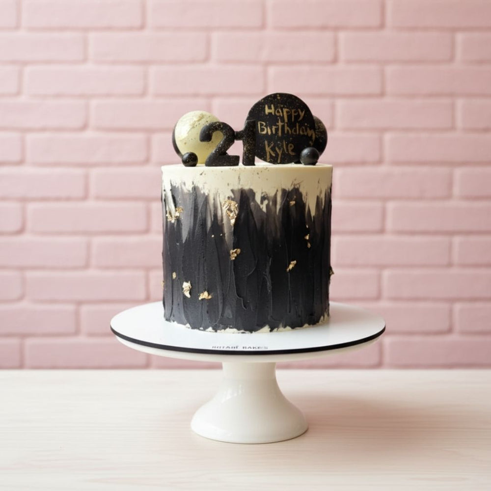 Black and gold birthday cake on a white stand with a pink brick wall background