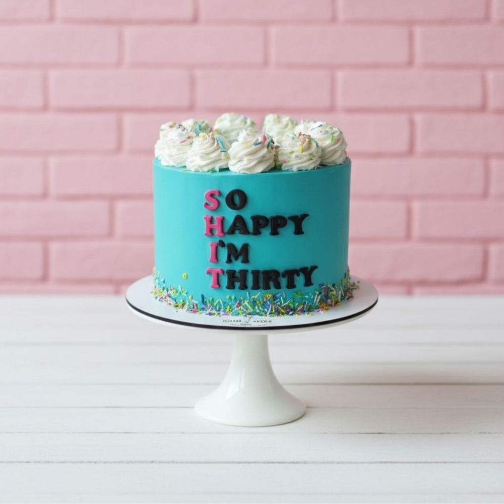 Blue birthday cake with 'So Happy I'm Thirty' text against a pink brick wall.