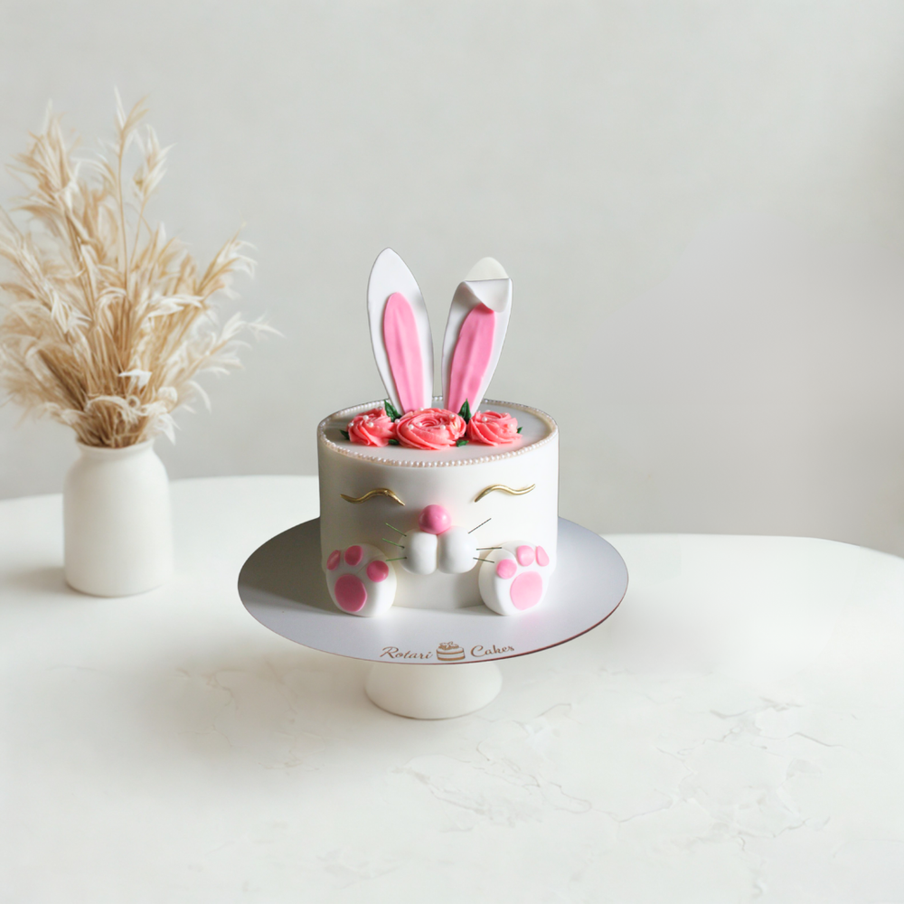 Small cake with bunny ears and pink flowers on a white surface with a neutral background