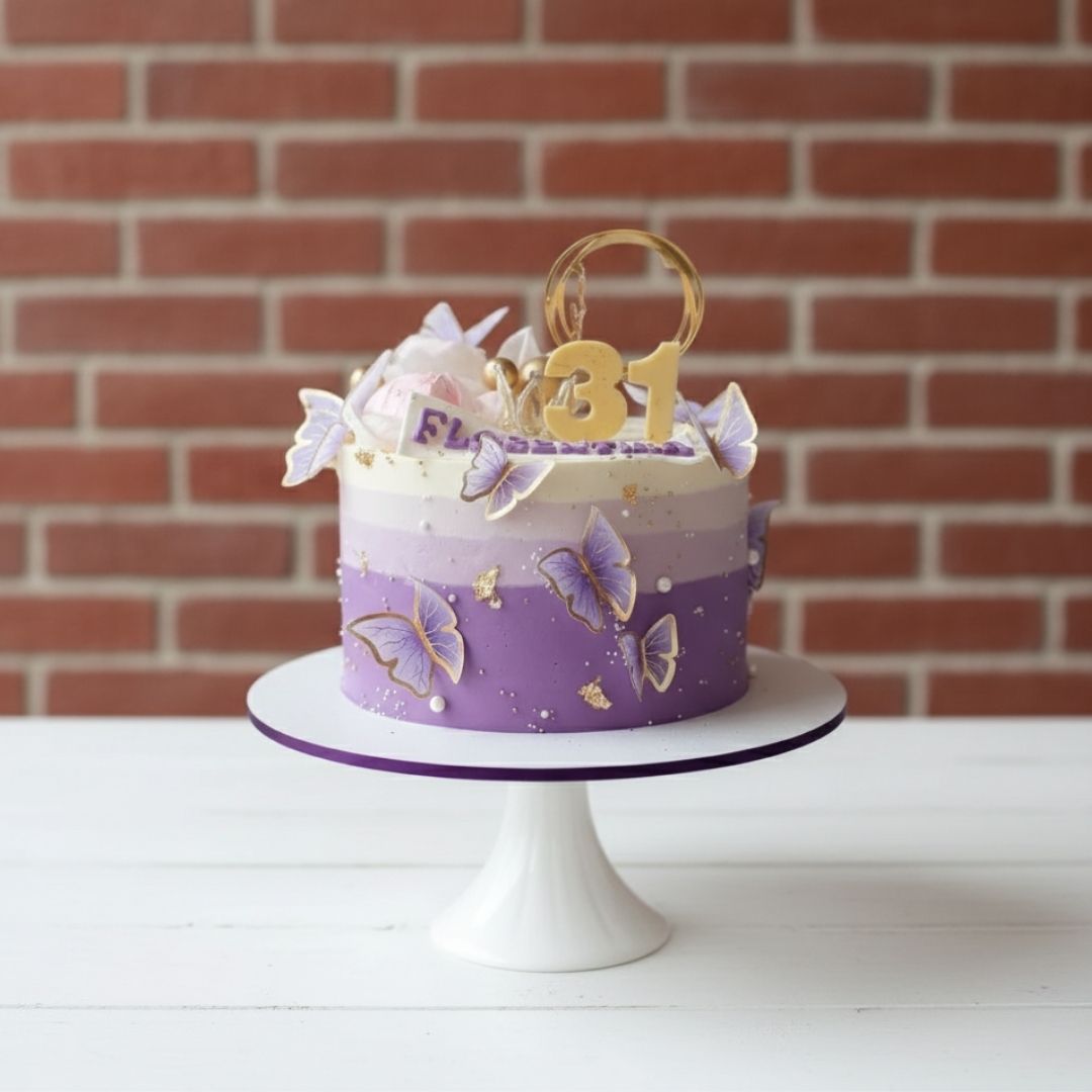 Purple birthday cake with butterfly decorations on a white stand against a brick wall.