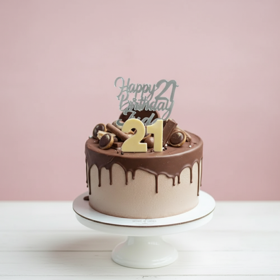Chocolate birthday cake with 'Happy 21st Birthday' topper on a white stand against a pink background