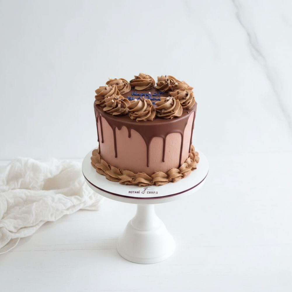 Chocolate cake with floral decorations on a white stand, surrounded by white flowers and fabric.