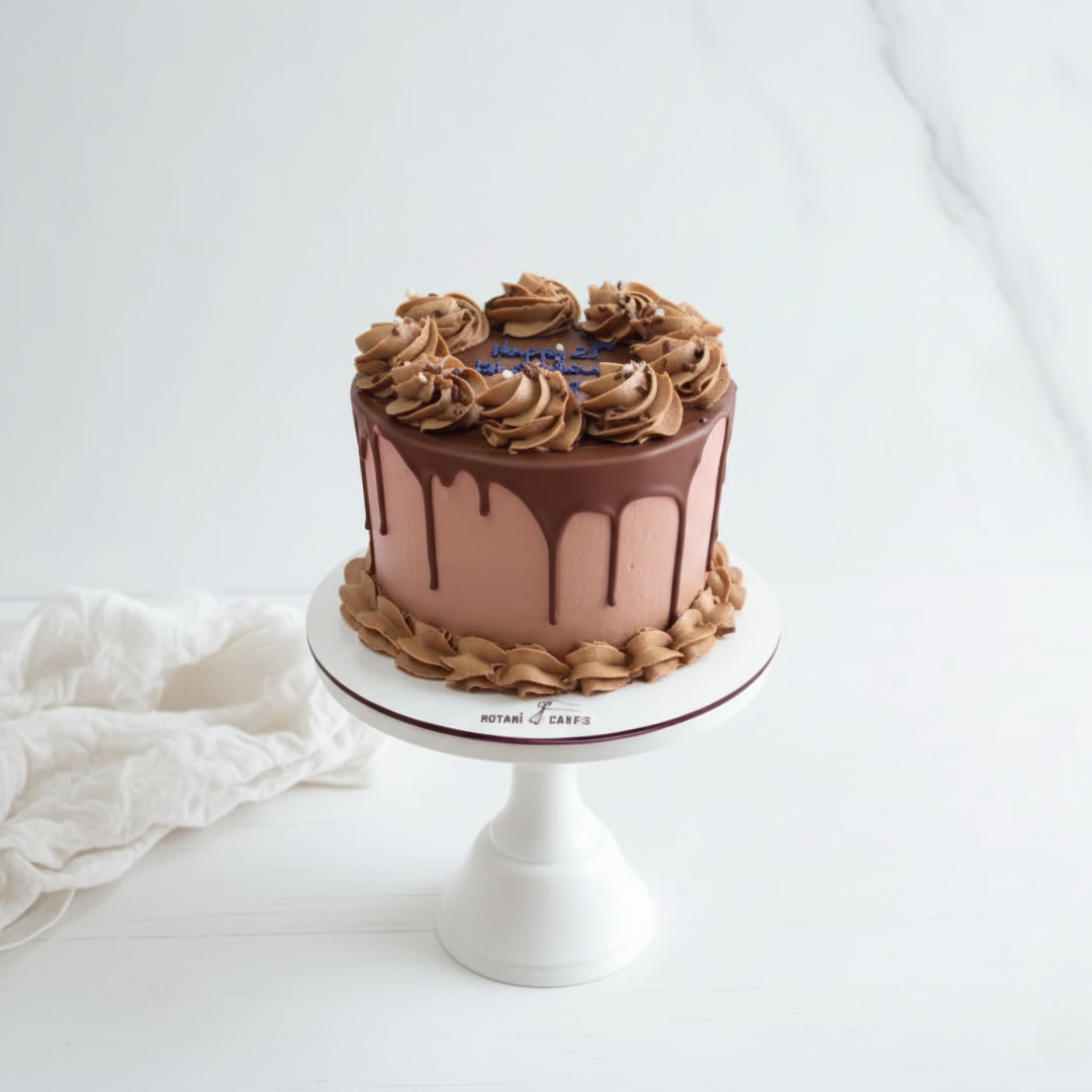 Chocolate cake with floral decorations on a white stand, surrounded by white flowers and fabric.