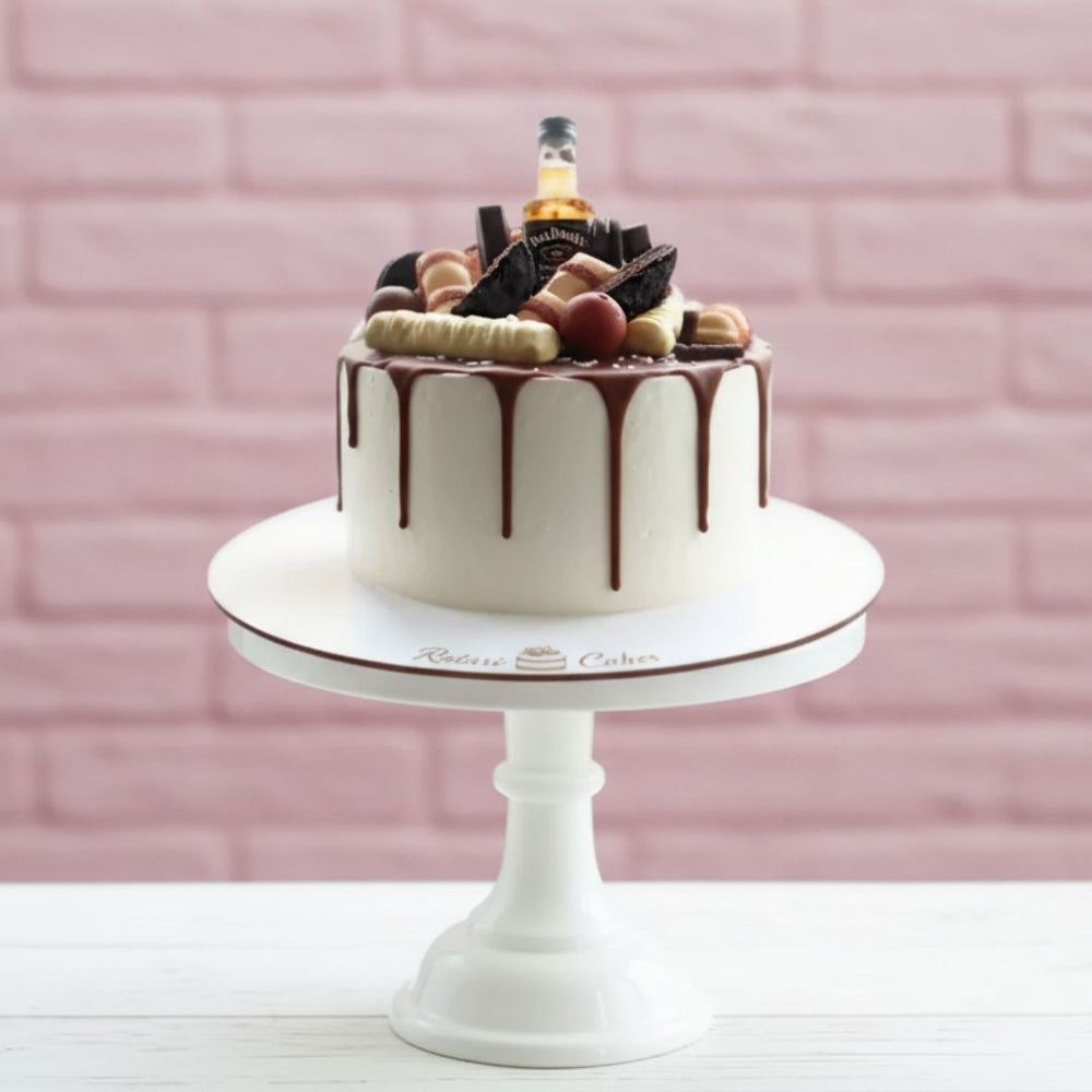 
                  
                    Decorative cake with chocolate drizzle on a white stand against a pink brick wall.
                  
                