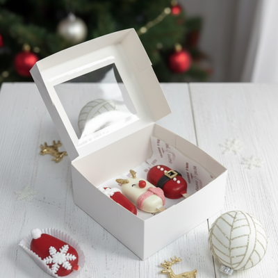 Decorative Christmas ornaments in a white box with a Christmas tree in the background