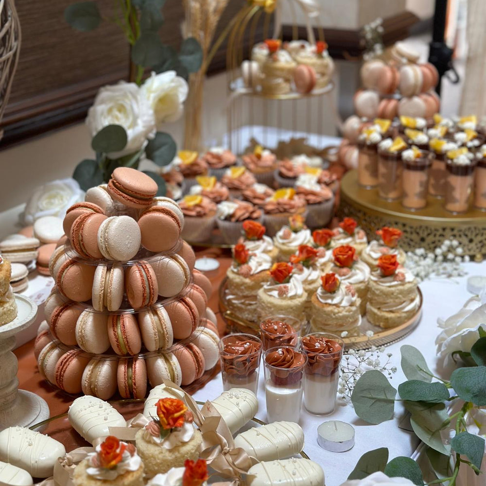 Decorative dessert table with macaron tower, small cakes, and flowers for corporate offices