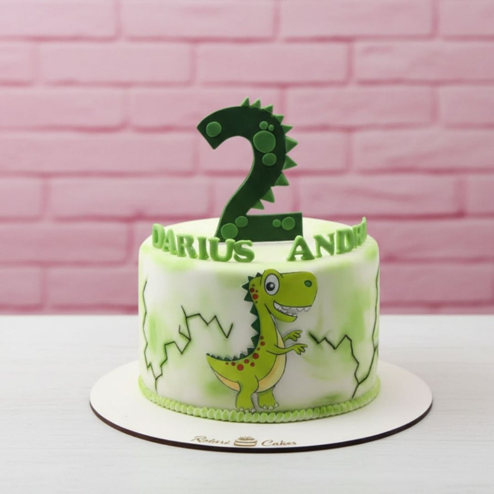 Green dinosaur-themed birthday cake with number 2 on a pink brick background