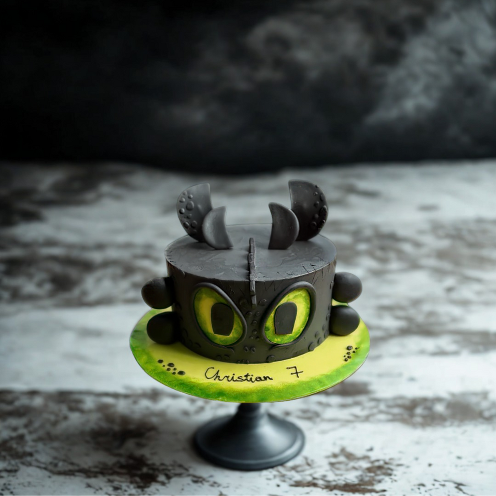 Cake designed like a dragon with green eyes and black scales on a rustic surface