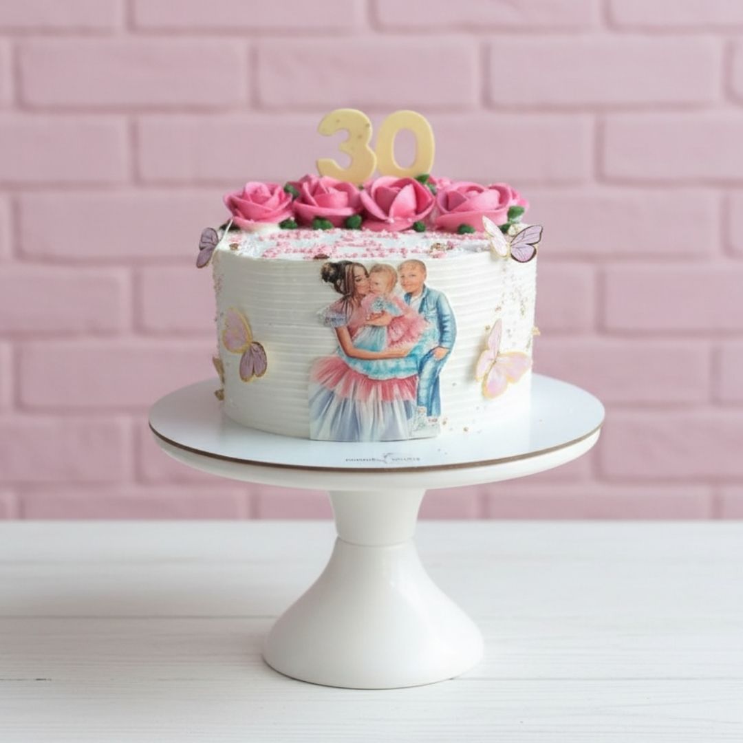 Birthday cake with pink flowers and number '30' on a white stand against a pink brick wall.