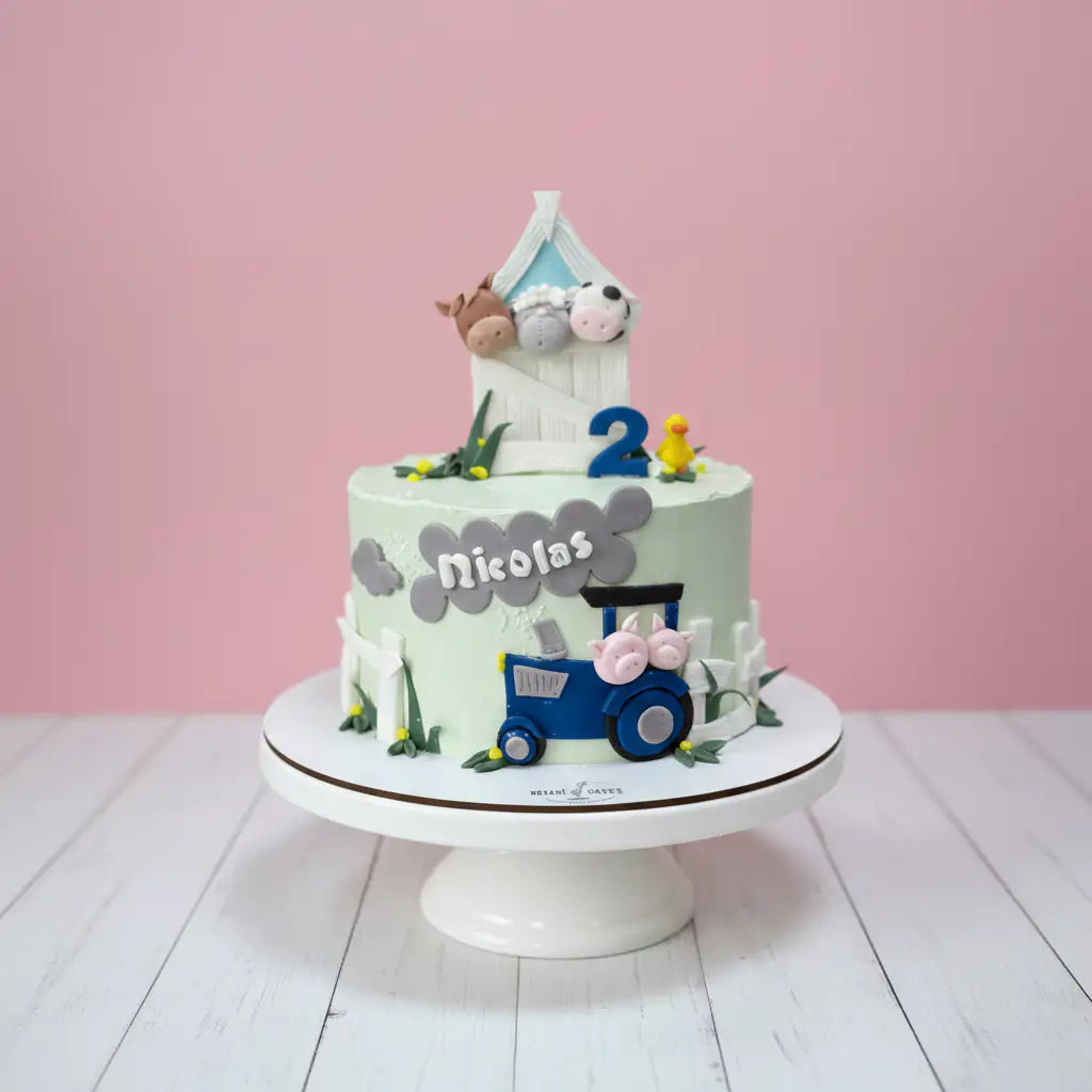 Children's birthday cake  of farm theme with a blue train design, number 2, and name 'Nicolas' on a pink background.