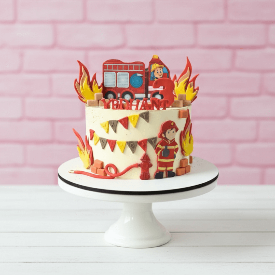 fireman theme Children's birthday cake with fire truck and firefighter design on a white stand against a pink brick wall.