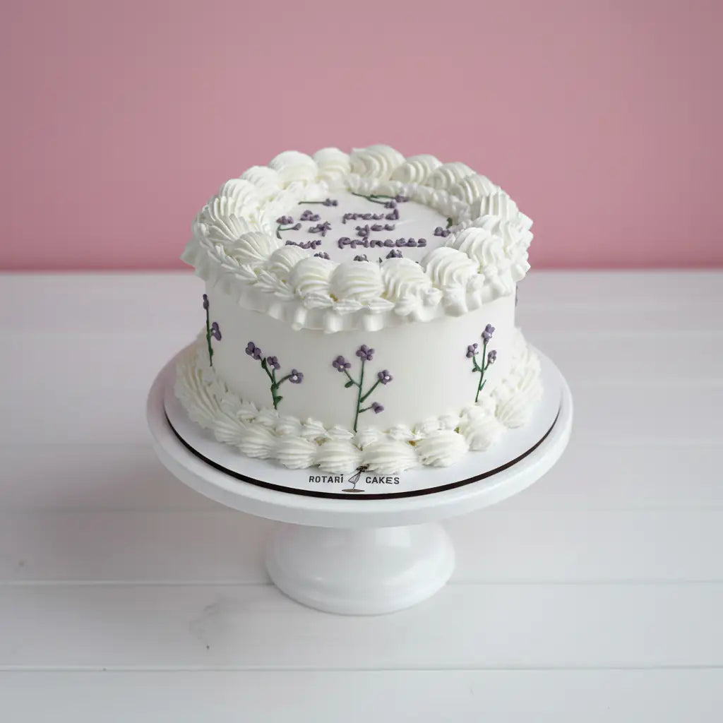 White cake with floral designs on a white stand against a pink background