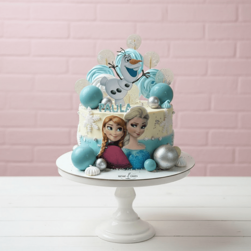 
                  
                    Frozen-themed cake with Elsa, Anna, and Olaf on a white stand against a pink brick wall.
                  
                