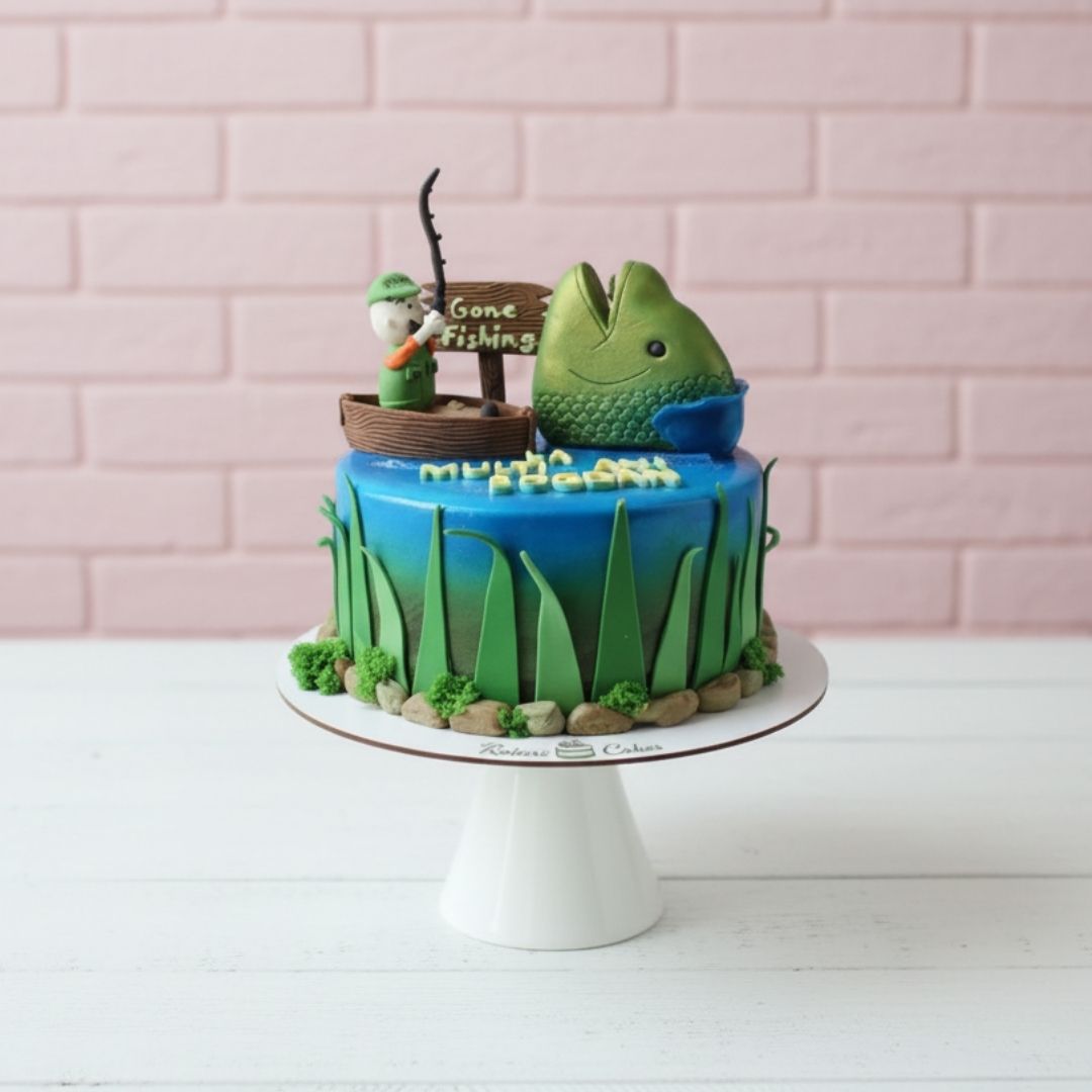 Fishing-themed cake with a fish and fishing rod decoration on a white stand against a pink brick wall.