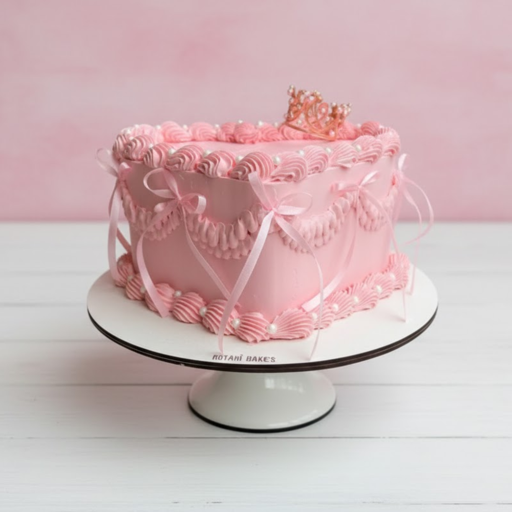 Pink heart cake with decorative elements on a white stand against a pink background