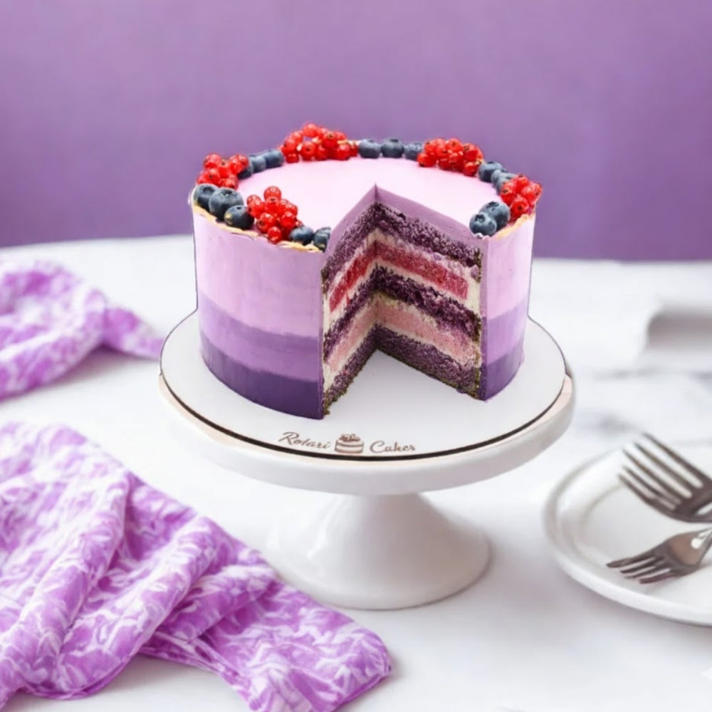 Layered cake with purple and red berries on a white cake stand against a purple background