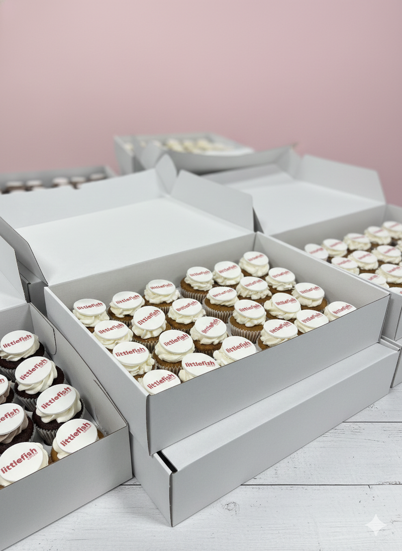 Open boxes containing cupcakes with visible branding on a light pink background