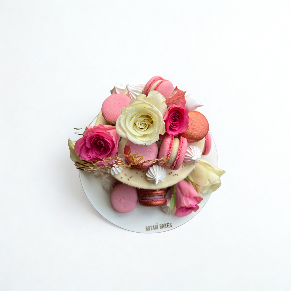 Decorative cake with pink and white flowers and macarons on a white background