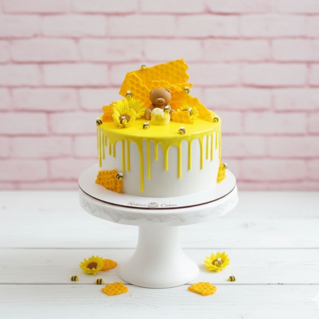 medovic White cake with yellow decorations on a white stand against a pink brick wall.