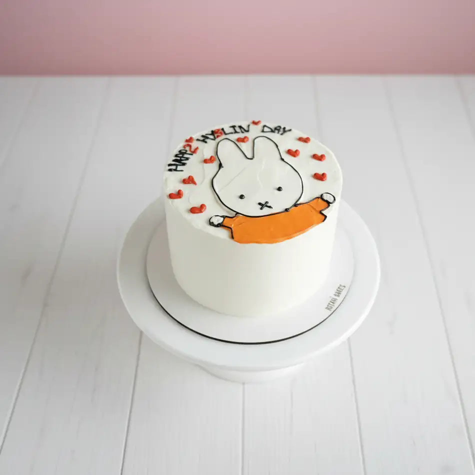 White miffy theme cake with cartoon character on a white plate against a pink background