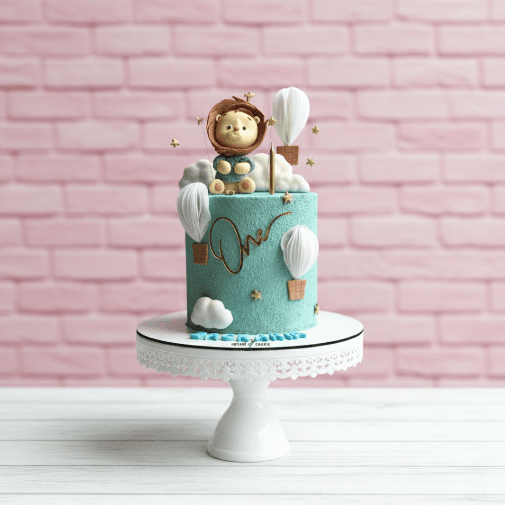 Decorative cake with a lion figurine and hot air balloons on a pink brick wall background