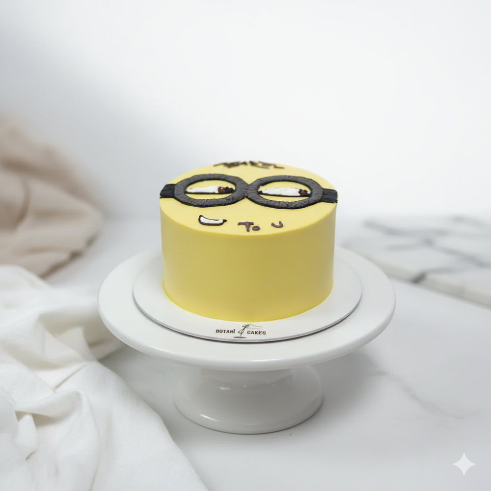 
                  
                    Yellow minion cake with black goggles on a white stand against a light background
                  
                