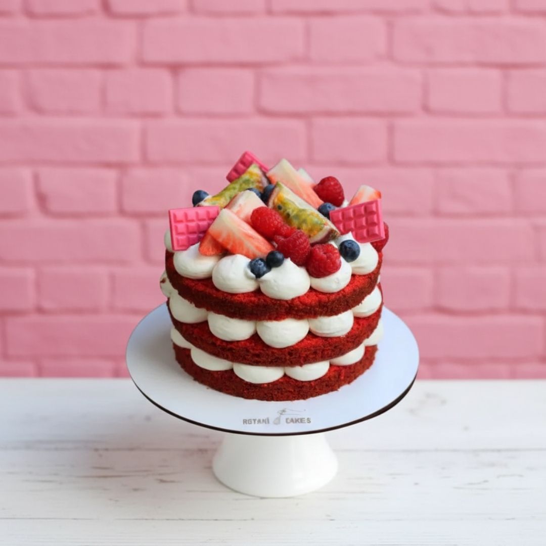 Naked Red velvet cake with fruit on a white stand against a pink brick wall