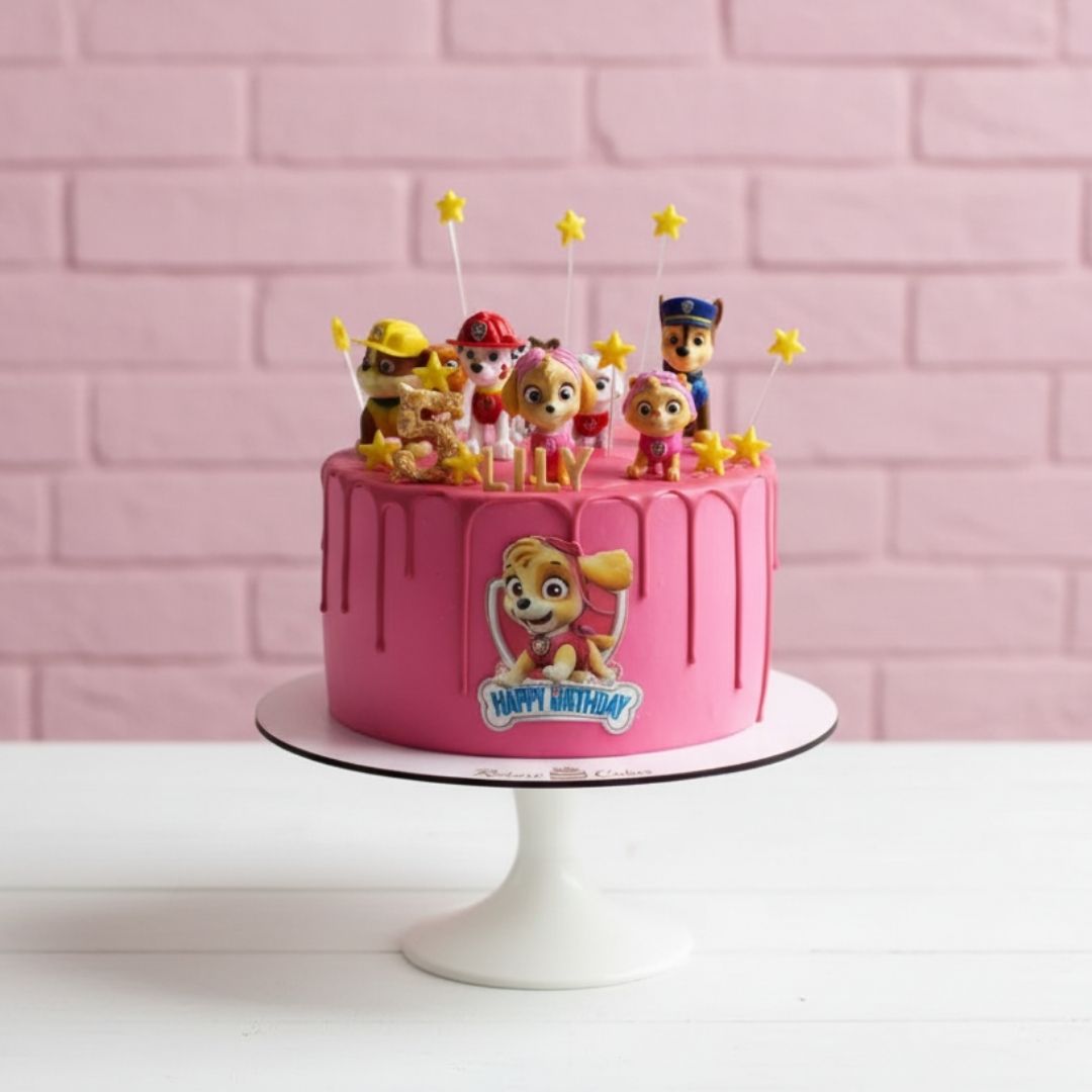 Pink paw patrol theme birthday cake with cartoon character figurines on a pink brick wall background