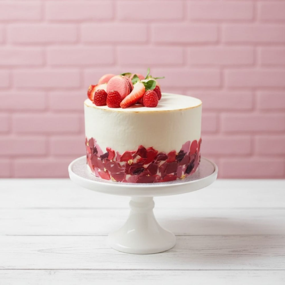 Decorative cake with berries on top on a white stand against a pink brick wall.