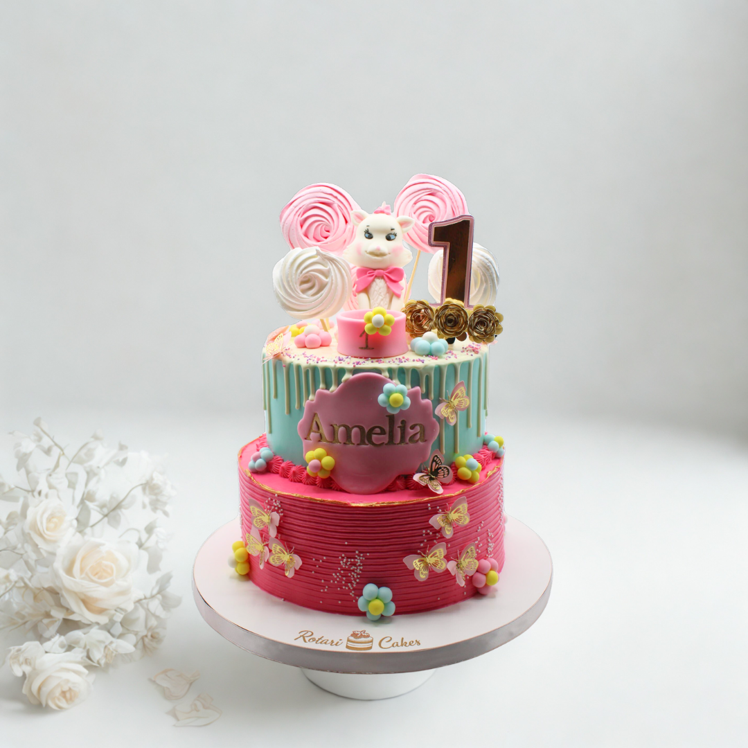 Two-tier birthday cake with pink and blue colors, decorated with a teddy bear and number '1' on a white background.