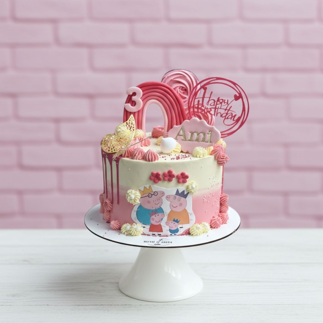 Pink birthday cake with Peppa Pig design on a white stand against a pink brick wall.