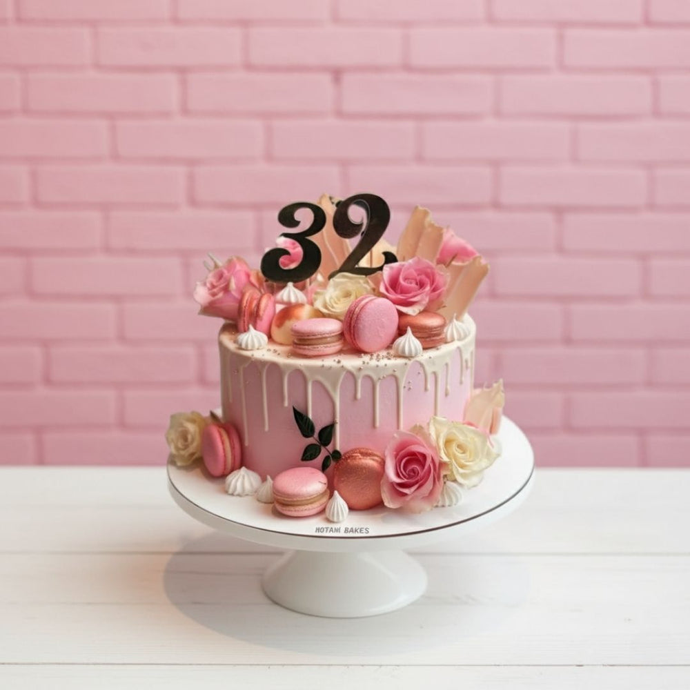 Pink birthday cake with flowers and number 32 against a pink brick wall.
