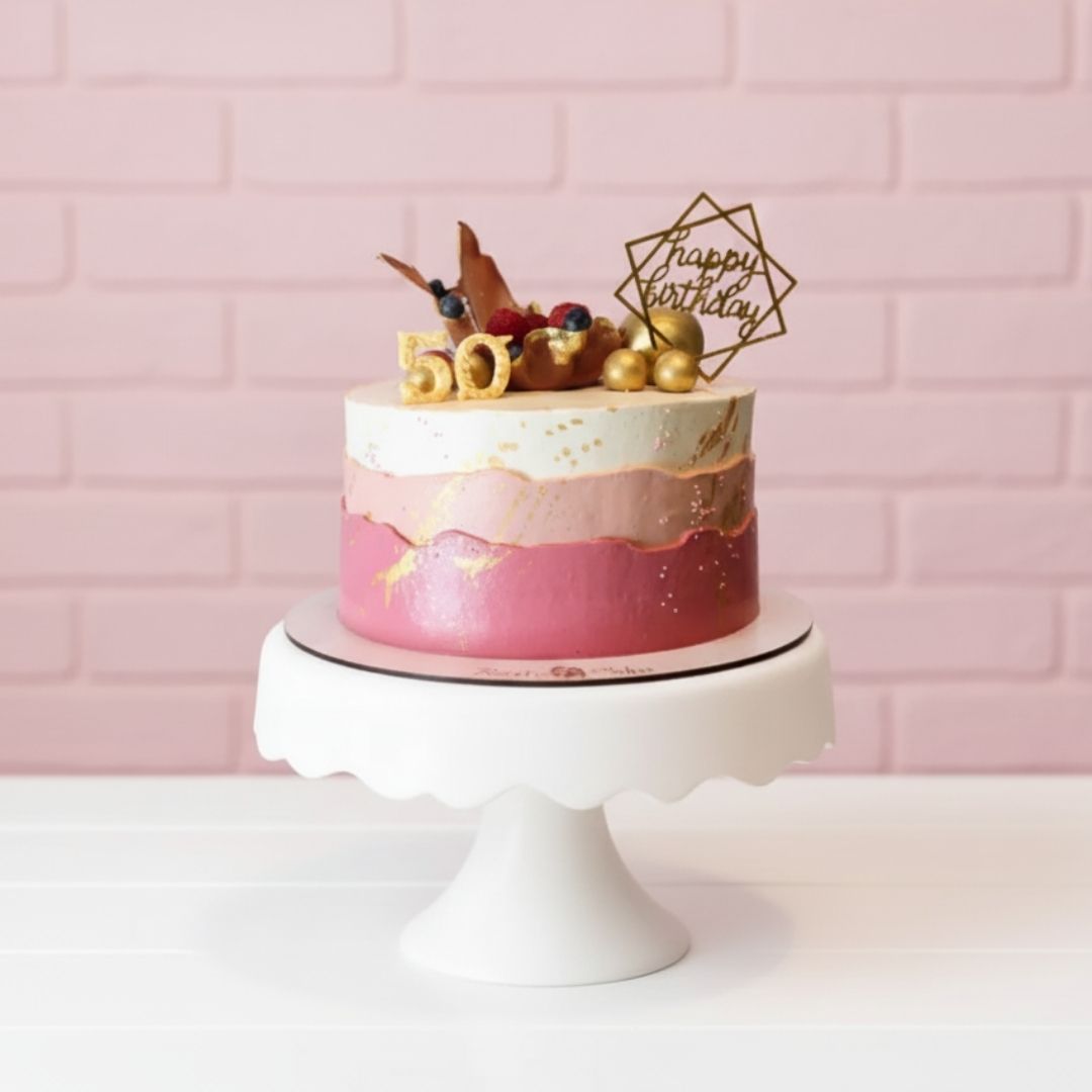 profiteroles decorative cake for 50th birthday with pink and gold layers on a white stand against a pink brick wall.