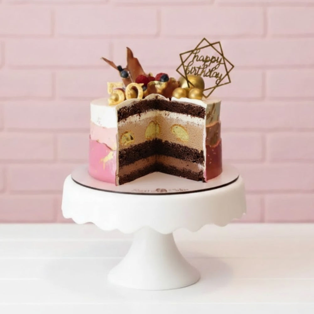 Layered birthday cake with a slice cut out on a white cake stand against a pink tiled wall.