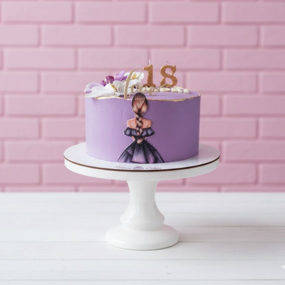 Purple birthday cake with a number 18 on a white cake stand against a pink brick wall.