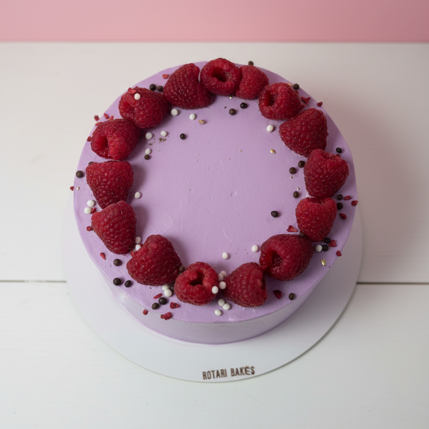 Purple cake with raspberries on a white stand against a pink background