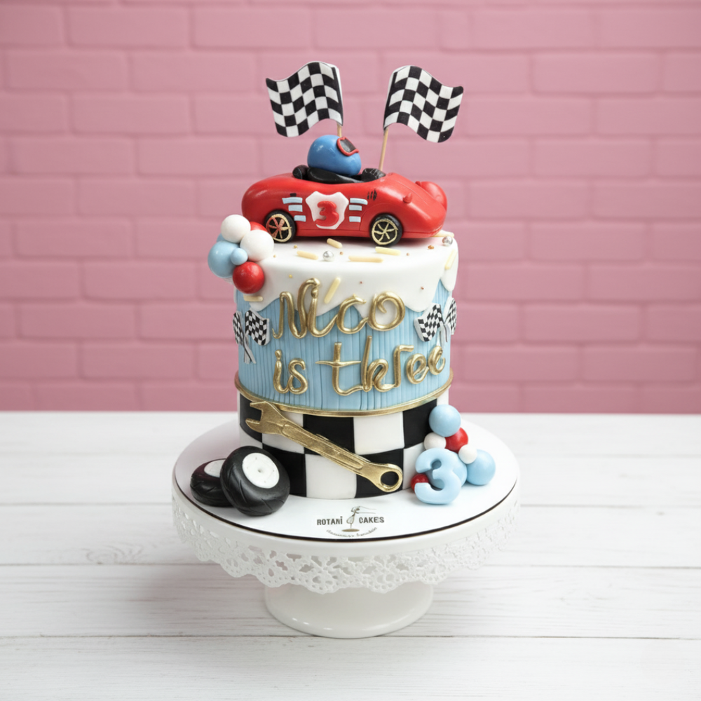 Decorative cake with a red car, checkered flags, and 'Nico is the best' text against a pink brick wall.