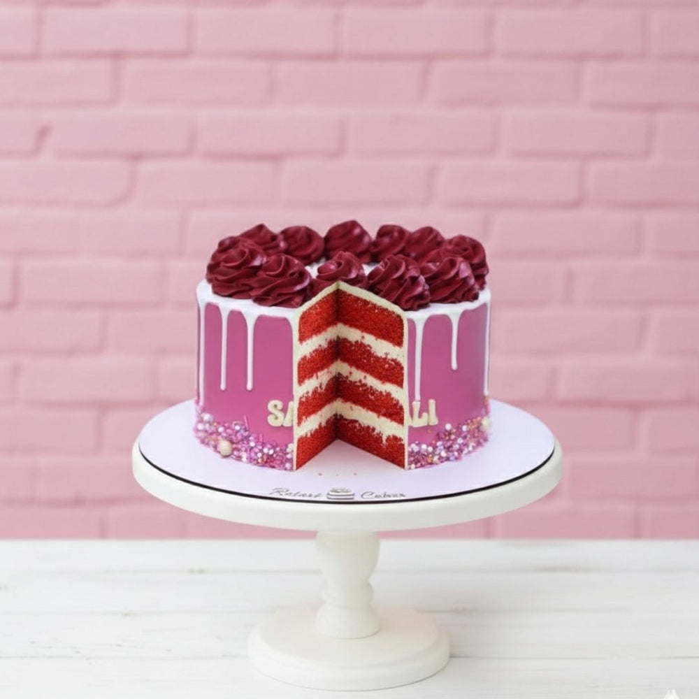 Decorative cake with red roses and pink frosting on a white stand against a pink brick wall.