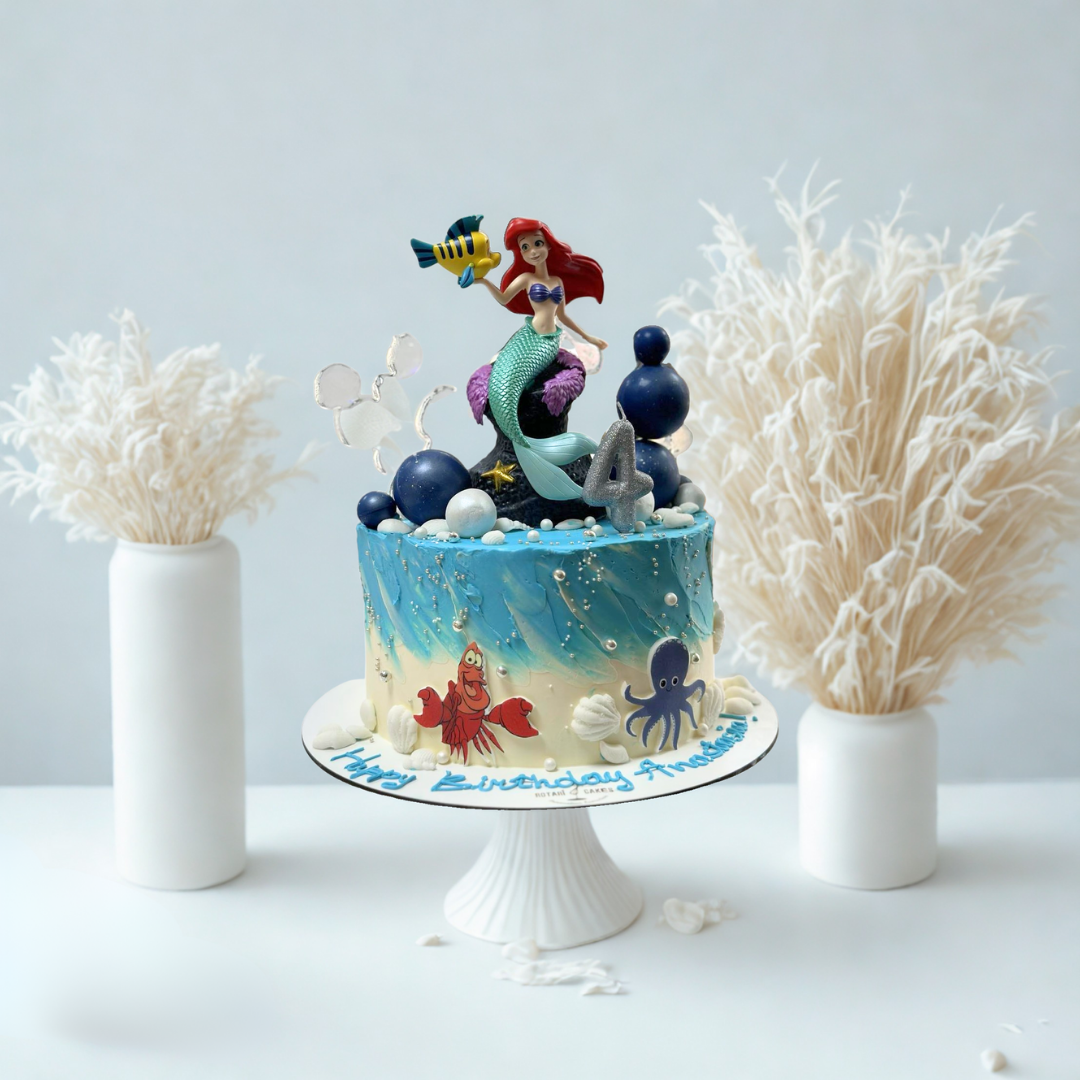 sea themed birthday cake with mermaid figurine and ocean elements on a white stand.