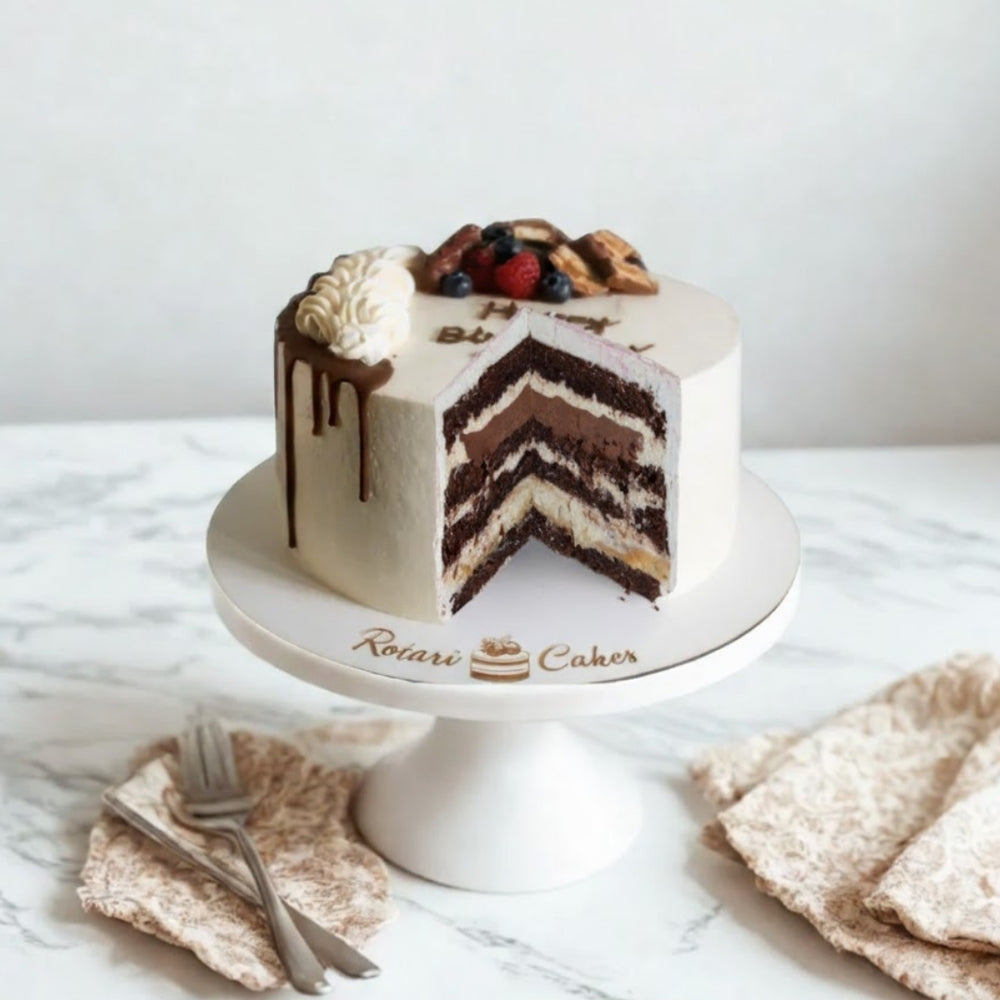
                  
                    Chocolate cake with white frosting on a white cake stand, featuring the brand 'Rotari Cakes'.
                  
                
