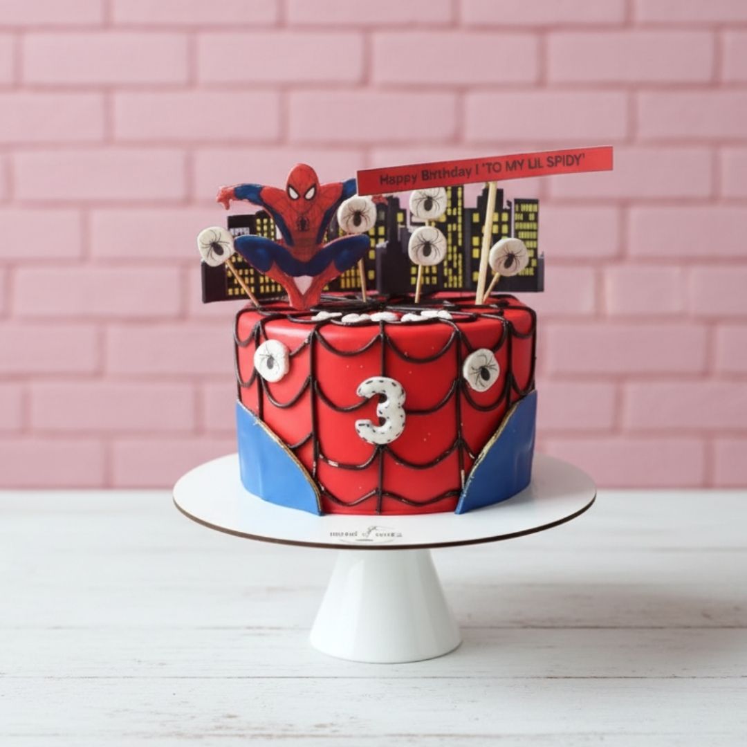Spider-Man themed birthday cake with number candles on a white stand against a pink brick wall.