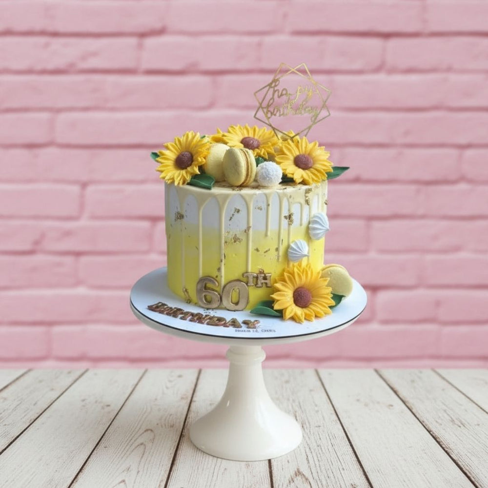 Yellow cake with sunflower decorations on a white stand against a pink brick wall.